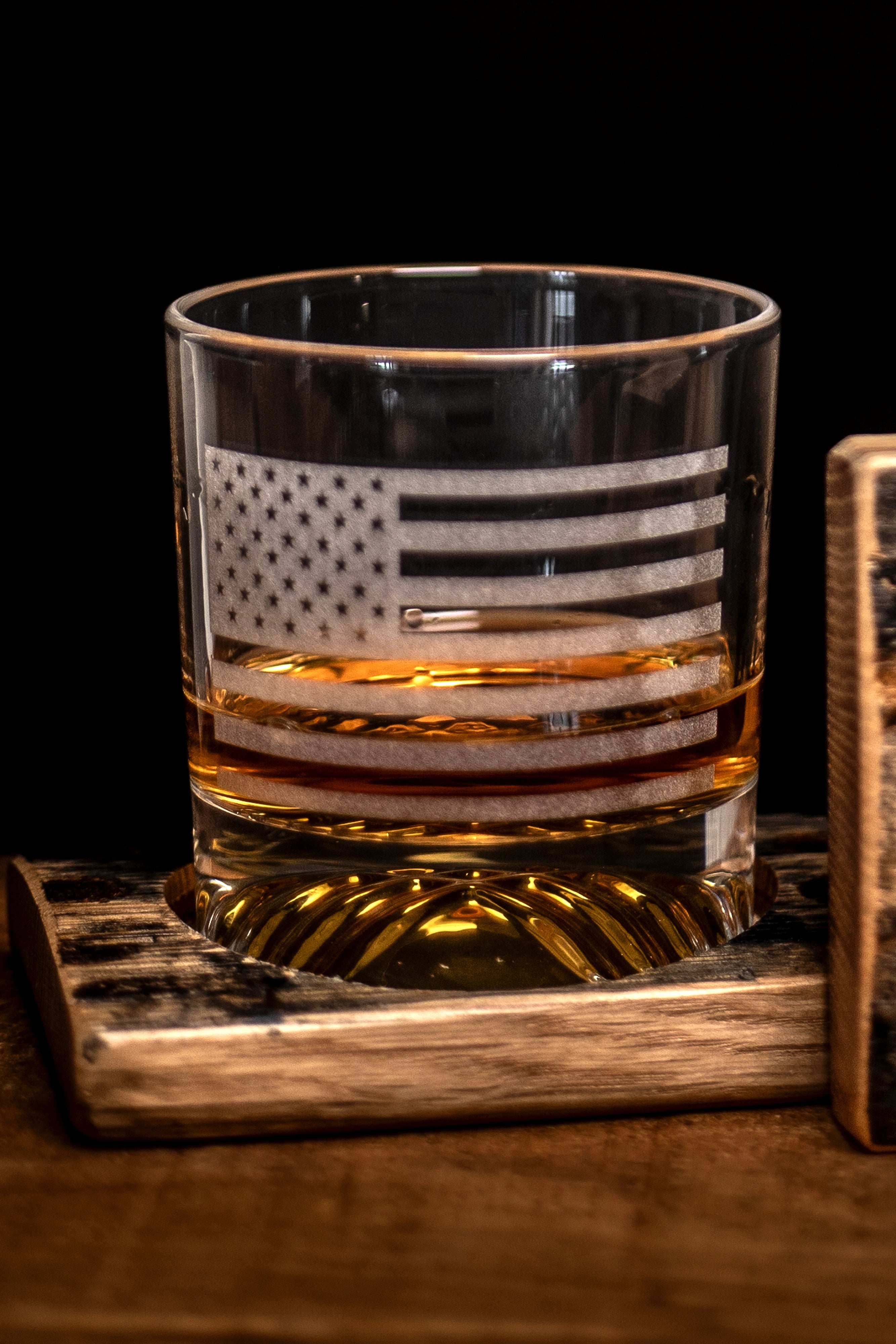 Rocks glass with American flag design filled on a bourbon barrel wooden coaster